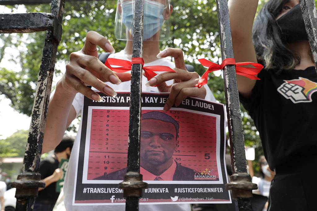 A demonstrator ties a red ribbon on a gate of the Department of Justice to symbolize their protest while holding a picture of U.S. Marine Lance Cpl. Joseph Scott Pemberton during a rally in Manila, Philippines, on Thursday, Sept. 3, 2020.