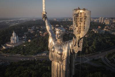Workers install the Ukrainian coat of arms on the shield in the hand of the country's tallest stature, the Motherland Monument, after the Soviet coat of arms was removed, in Kyiv, Ukraine, Sunday, Aug. 6, 2023.
