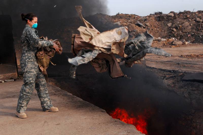 An airman tosses unserviceable uniform items into the Joint Base Balad, Iraq, burn pit in this March 2008 file photo from the U.S. Air Force.