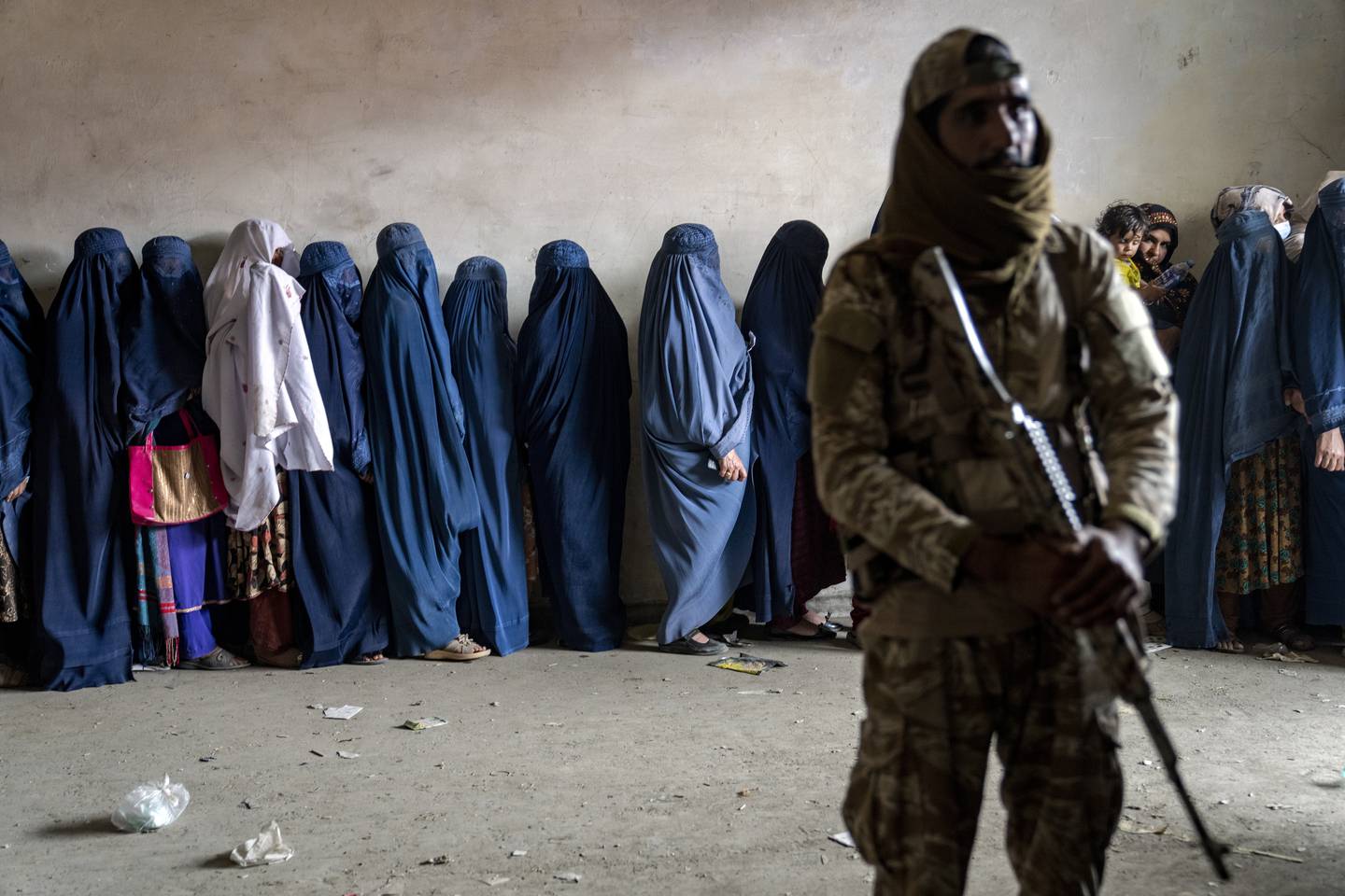 A Taliban fighter stands guard as women wait to receive food rations distributed by a humanitarian aid group in Kabul, Afghanistan, Tuesday, May 23, 2023.