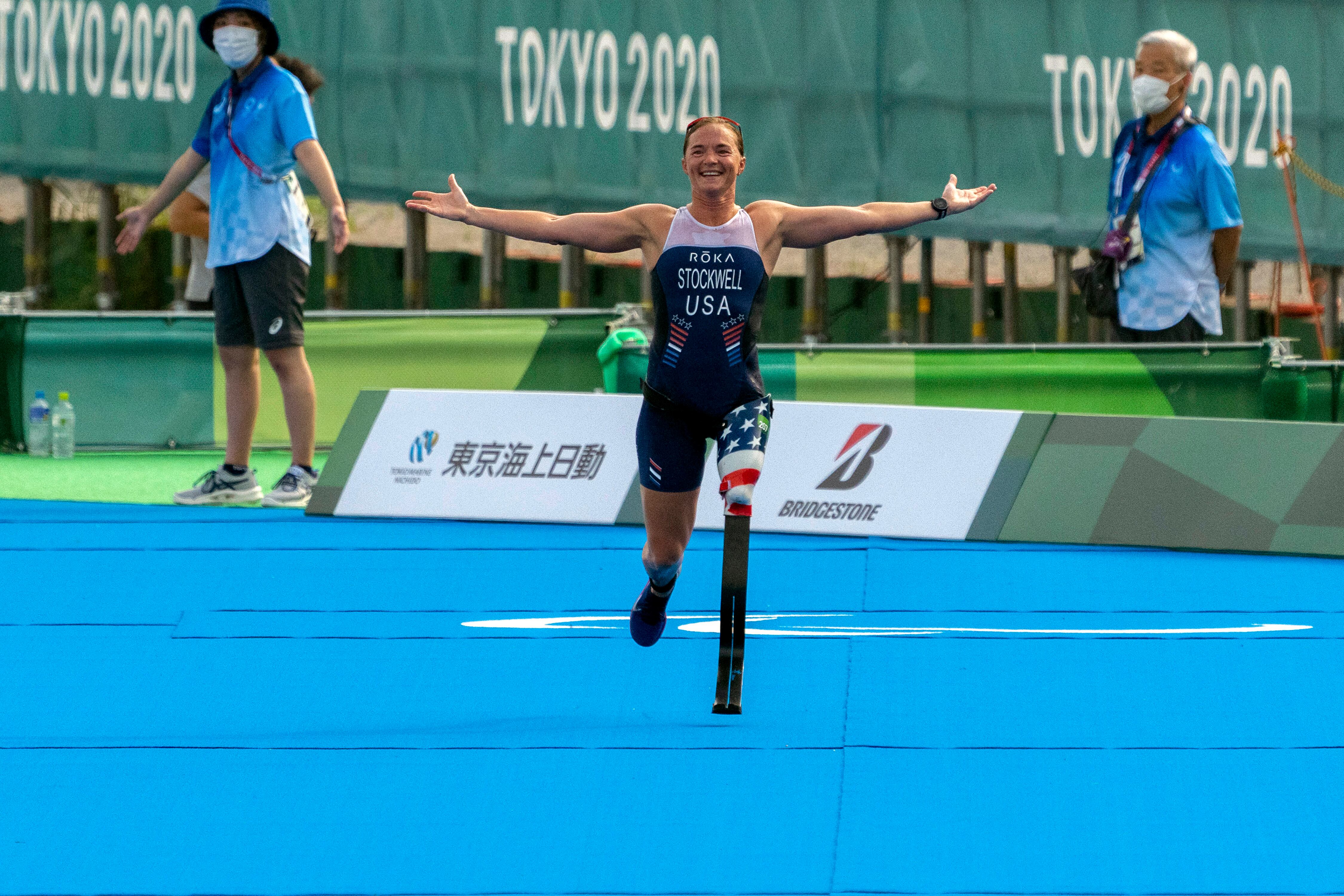 Paralympian Melissa Stockwell smiles and runs with her arms open to the finish line of the Women's Triathlon during the 2020 Tokyo Olympics.