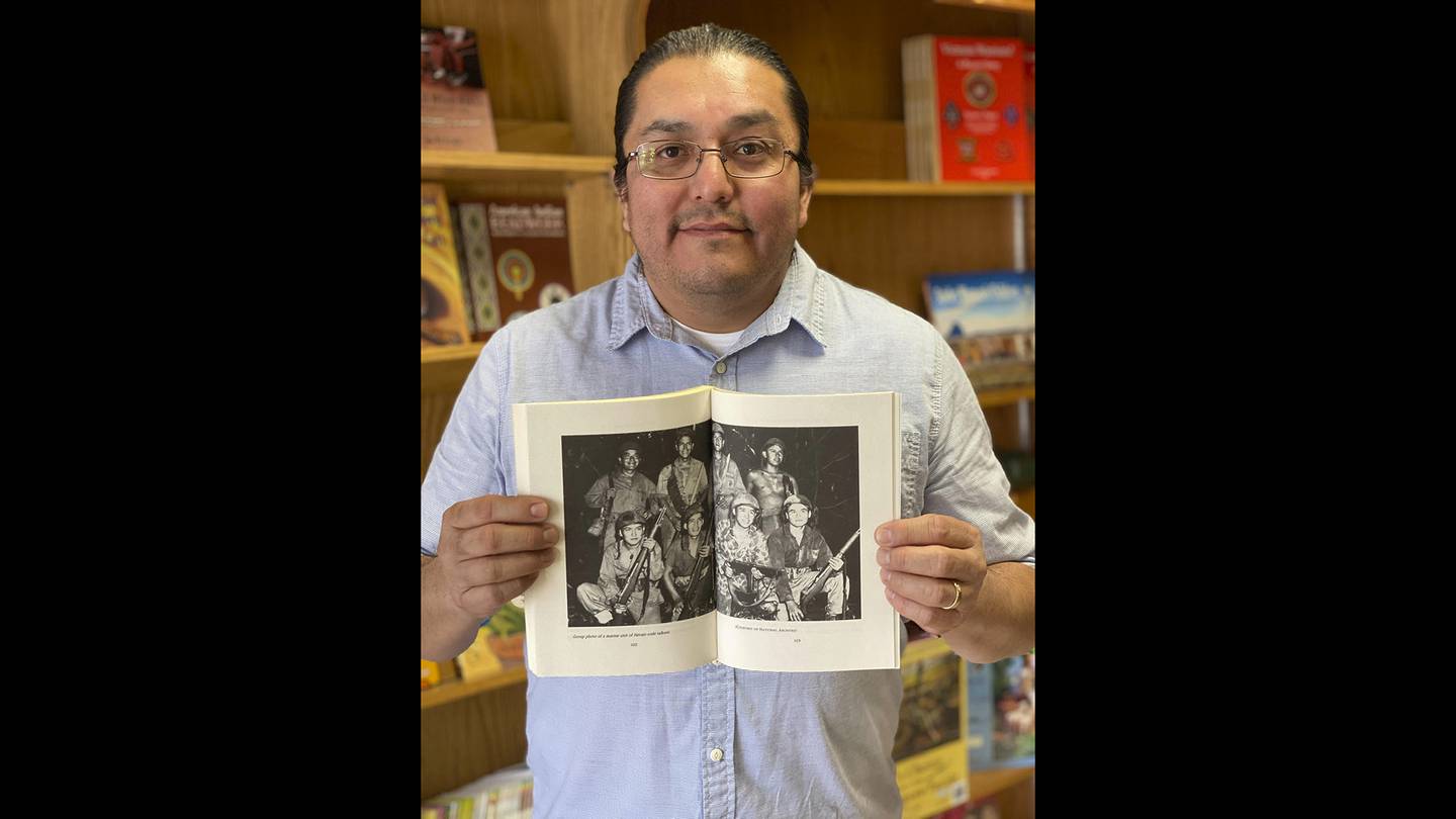 This Nov. 8, 2019, photo shows LT Goodluck holding a book with a photo of his grandfather, John V. Goodluck, first row, third from left holding a machine gun, with other Navajo Code Talkers at the Navajo Museum in Window Rock, Ariz.