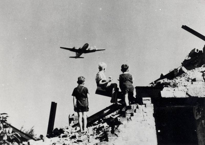 Children look on as a plane flies overhead. In 1948, the U.S. reportedly delivered some 13,000 tons of cargo and took off more than 89,000 times, totaling more than 600,000 hours of flight.